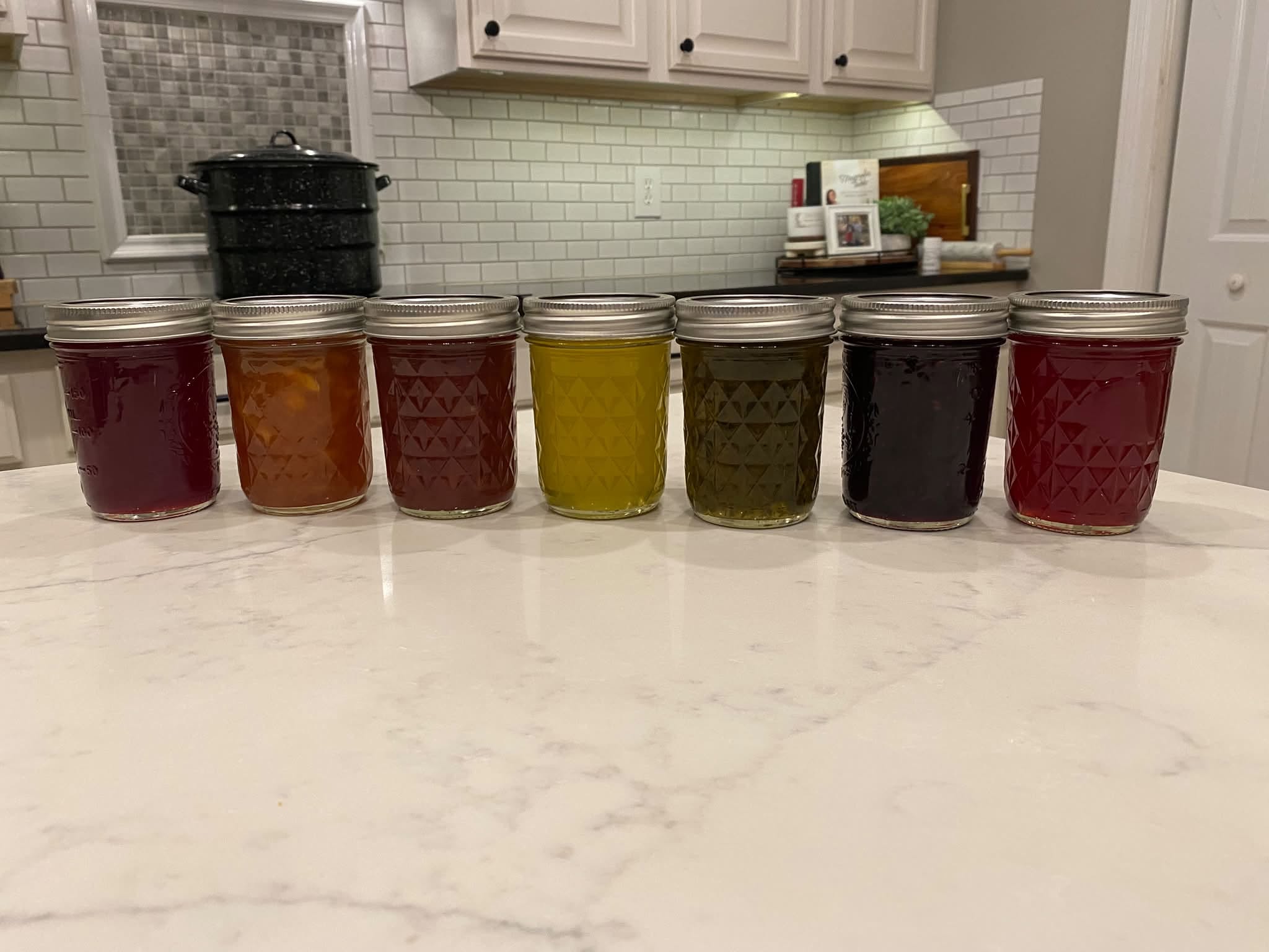 Seven colorful jars of The Preserved Peach’s homemade jams and jellies in the preserving kitchen